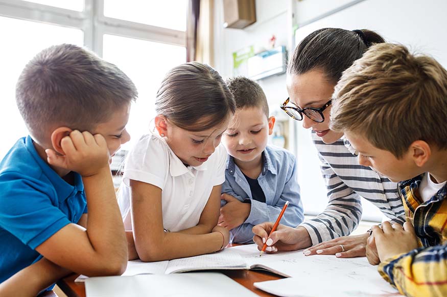 A small group of children sat together with their teacher in a classroom.